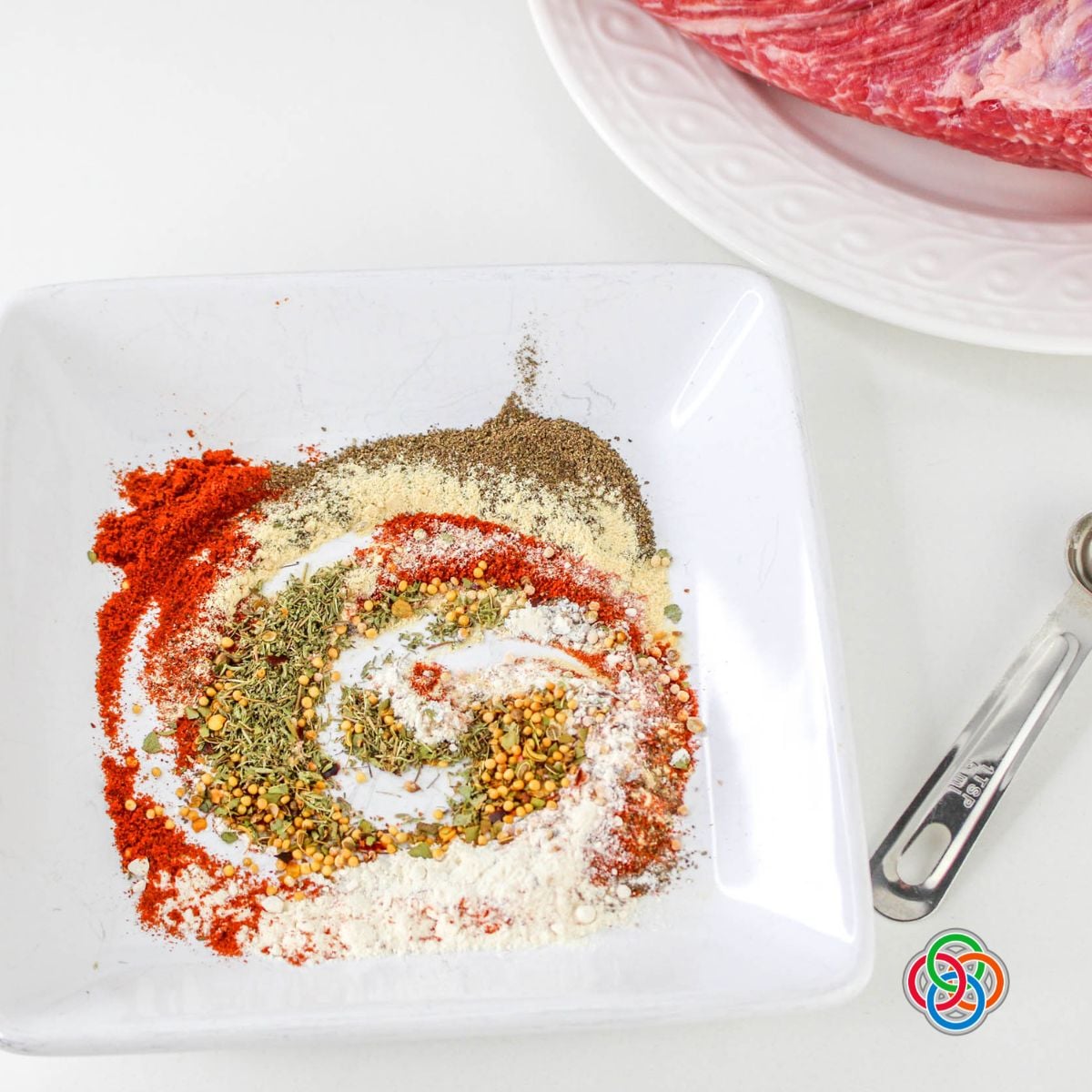 Plate with mixed spices including paprika, garlic powder, onion powder, thyme, and pepper used to create a homemade seasoning rub for corned beef brisket.