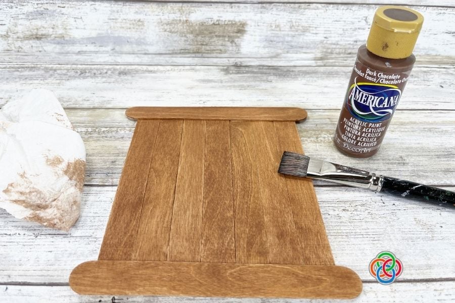 Craft stick sign painted with dark brown acrylic paint and brush to create a rustic stained look for a St. Patrick’s Day shamrock craft.