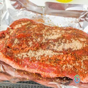 Raw corned beef brisket covered with a homemade seasoning rub on aluminum foil before cooking in an air fryer.