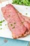 Sliced of cooked corned beef with parsley garnish on a white plate.