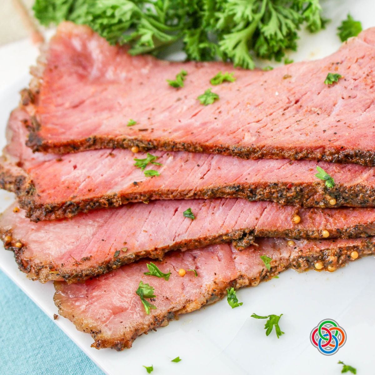 Slices of cooked corned beef brisket with a seasoned crust garnished with parsley on a white plate.