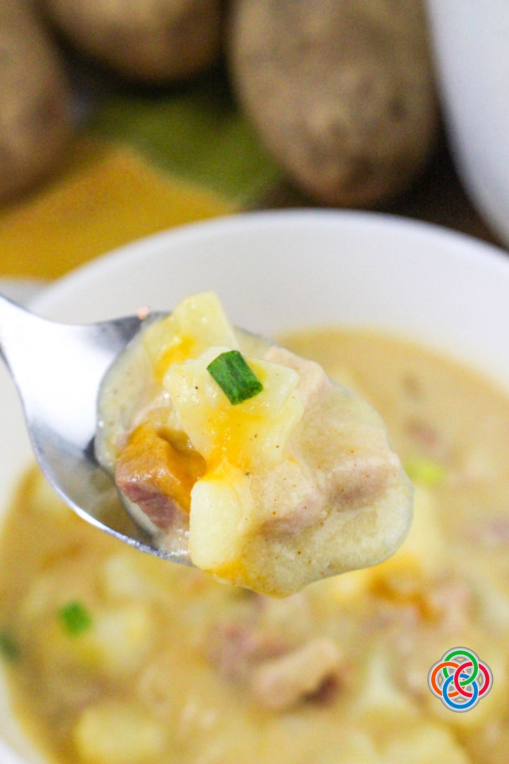 Close-up of a spoonful of creamy cheddar ham and potato soup with chunks of potato, ham, melted cheese, and a piece of green onion on top.