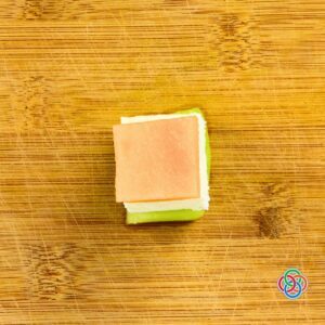 Overhead view of a single Irish flag appetizer stack made with a cube of honeydew, a layer of feta cheese, and a cube of cantaloupe arranged on a wooden cutting board.