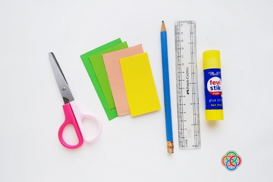 Scissors, colored craft paper, pencil, ruler, and glue stick arranged on a white background for a paper tulip craft project.