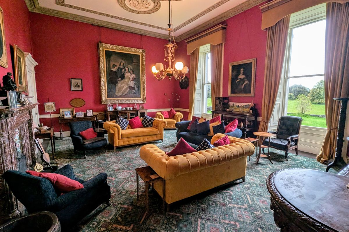The Drawing Room in Temple House in County Sligo | Irish American Mom Elegant drawing room inside Temple House Estate in County Sligo, Ireland, featuring red walls, antique furniture, historic portraits, and tall windows overlooking the countryside.
