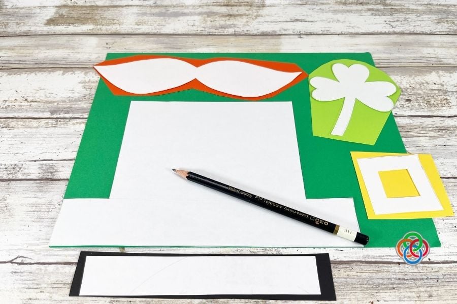 Printable template pieces for leprechaun hat, mustache, shamrock, and buckle traced onto colored cardstock with pencil during a paper plate leprechaun craft tutorial.