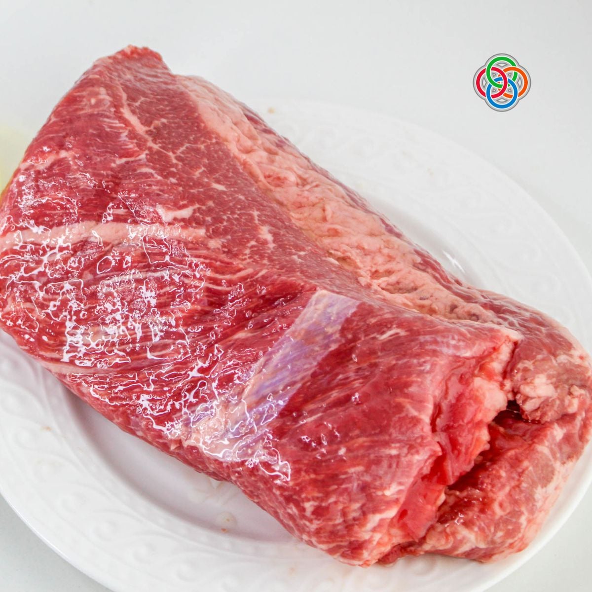 Raw uncooked corned beef brisket on a white plate ready to be seasoned and cooked in an air fryer.