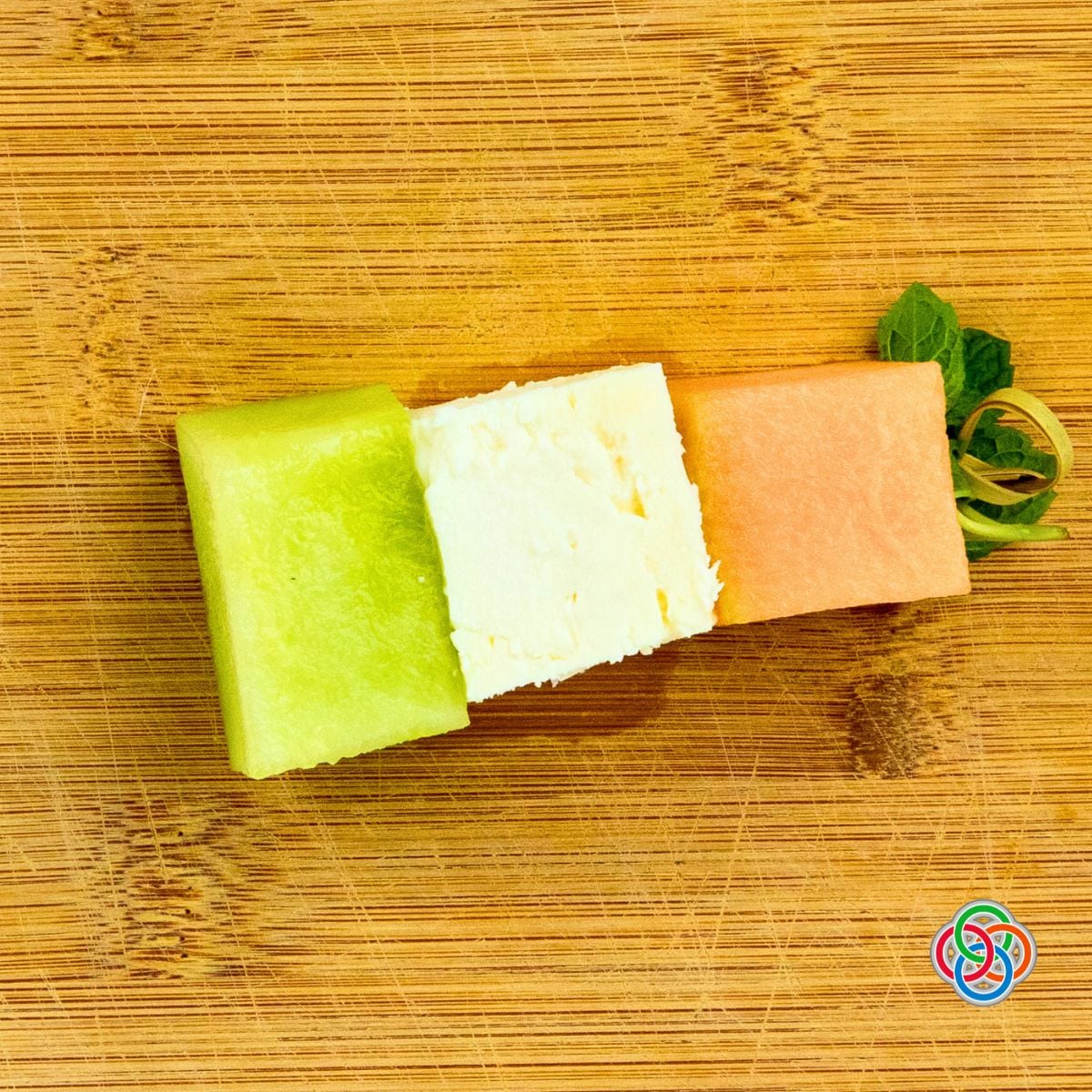 Overhead view of an Irish flag appetizer stack made with honeydew, feta cheese, and cantaloupe secured with a decorative cocktail stick on a wooden cutting board.