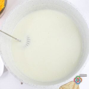 Milk being whisked into a roux in a pot to create a smooth, creamy base for ham and potato soup.