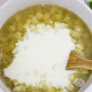 Creamy white sauce being added to a pot of diced potatoes and broth, combining to make a thick ham and potato soup.