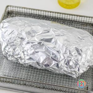 Corned beef brisket wrapped in aluminum foil and placed in an air fryer basket before cooking.