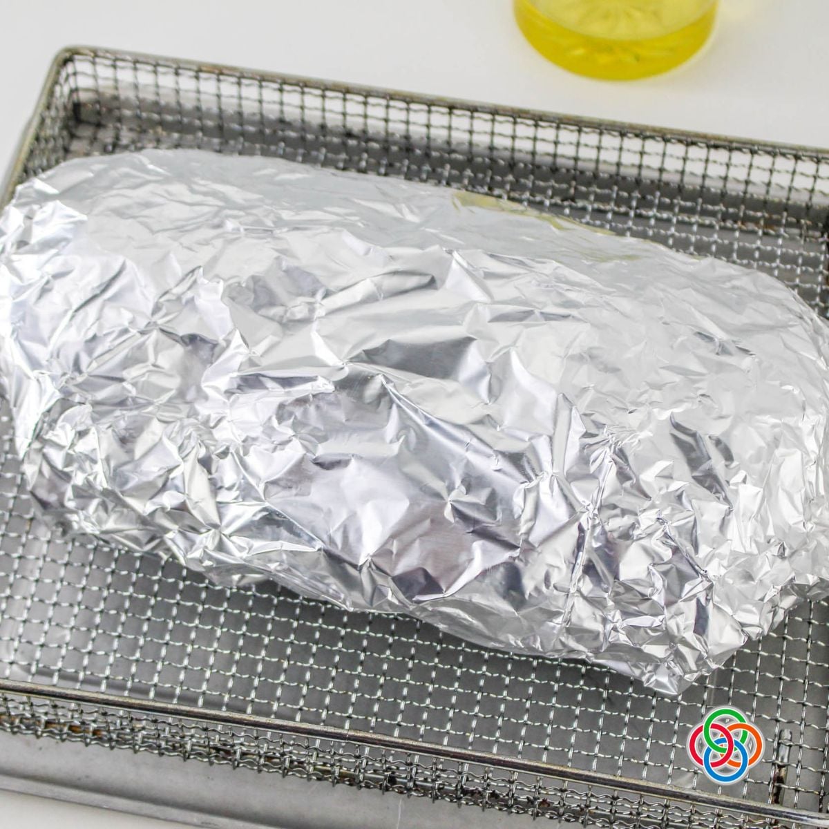 Corned beef brisket wrapped in aluminum foil and placed in an air fryer basket before cooking.