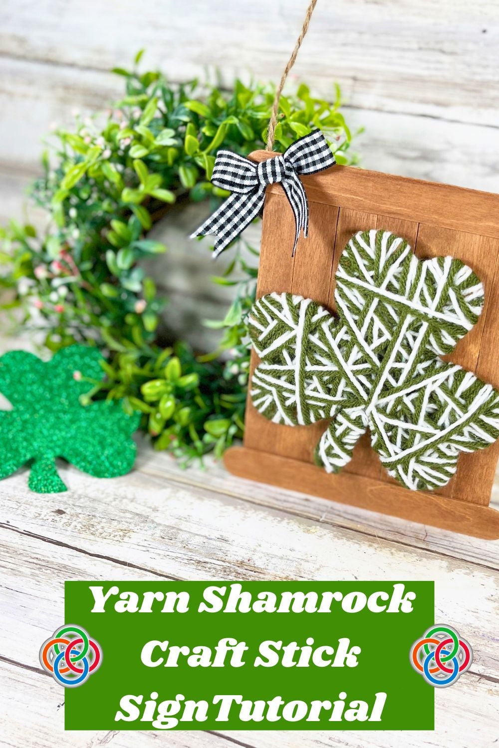 Yarn wrapped shamrock attached to a rustic craft stick sign with a gingham bow and twine hanger for a St. Patrick’s Day craft tutorial display.