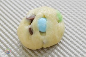 Ball of cake mix cookie dough with pastel M&M candy and chocolate chips placed on a baking sheet, ready for baking.