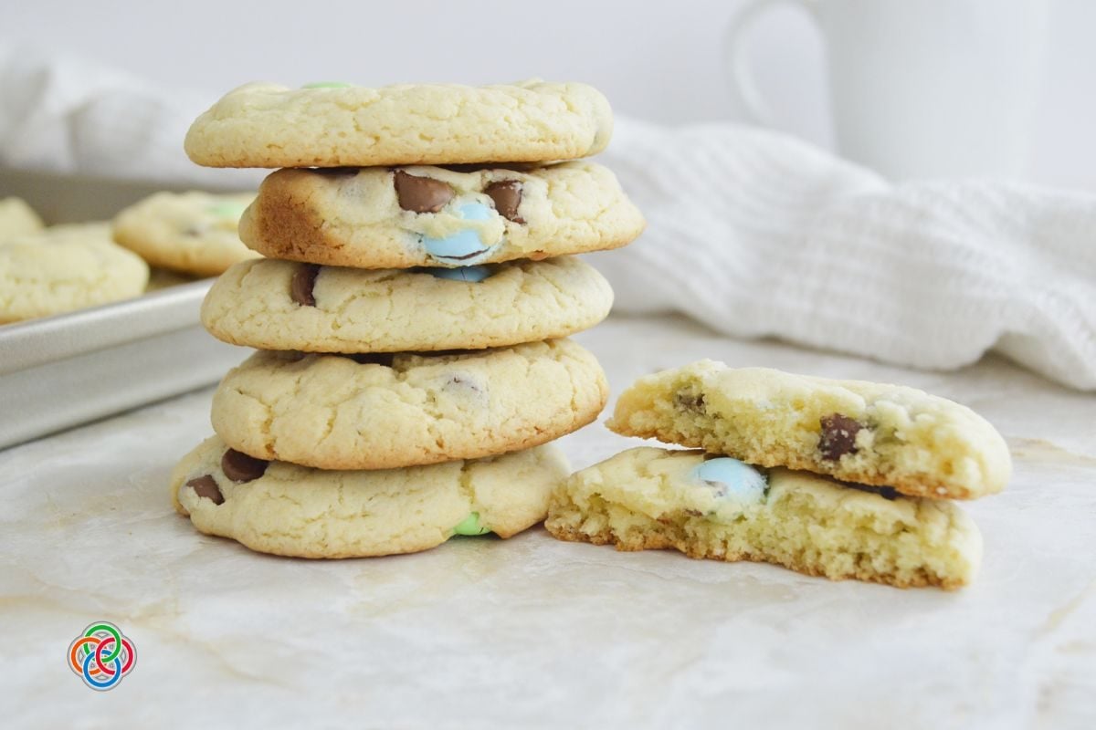 Stack of soft spring cake mix cookies with pastel M&M candies and chocolate chips, with one cookie broken open to show the chewy interior.