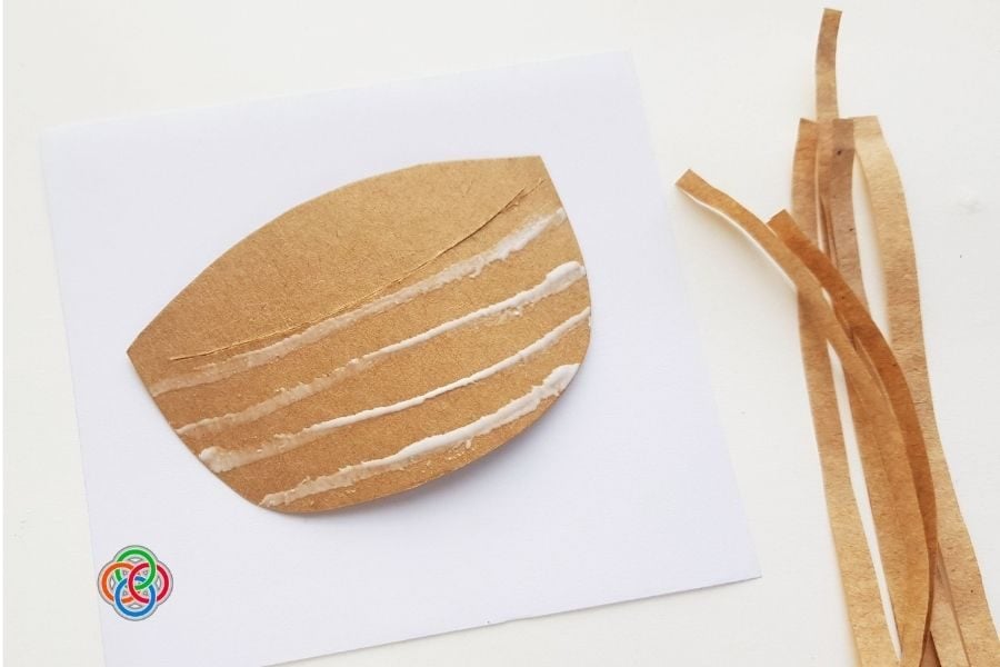 Brown cardstock basket base with horizontal lines of glue applied, ready for weaving paper strips, with cut paper strips placed beside it.