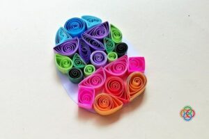 Colorful quilled Easter egg made with bright paper coils in pink, purple, blue, green, and orange arranged in decorative patterns on a white background.
