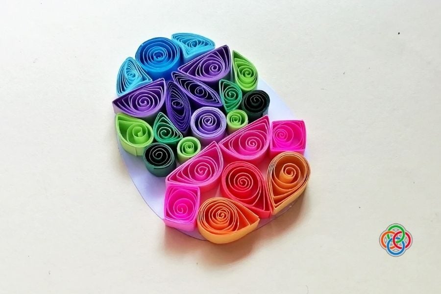 Colorful quilled Easter egg made with bright paper coils in pink, purple, blue, green, and orange arranged in decorative patterns on a white background.