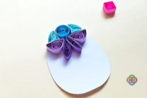 Early stage of a quilled Easter egg showing a few colorful paper shapes arranged at the top of a white egg template.