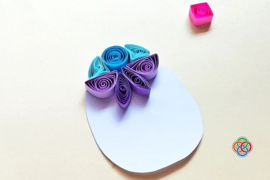 Early stage of a quilled Easter egg showing a few colorful paper shapes arranged at the top of a white egg template.