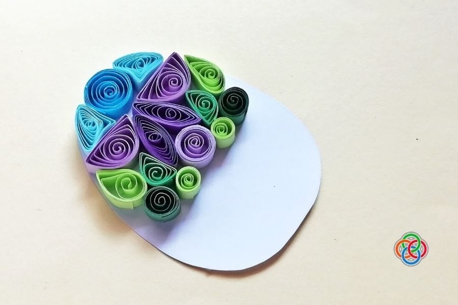 Partially decorated quilled Easter egg showing colorful paper coils and shapes arranged on the top section of a white egg template.