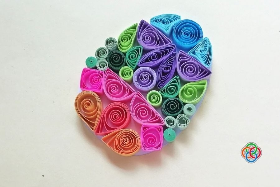 Completed quilled Easter egg made with colorful paper coils and shapes arranged in a vibrant decorative pattern on a white background.