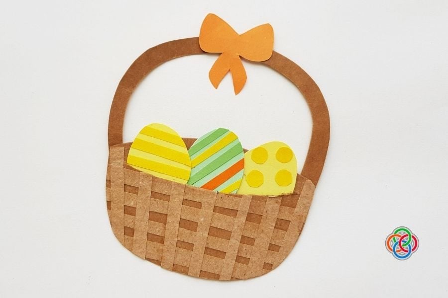Finished paper Easter basket craft with a woven brown base, handle with bow, and three colorful decorated Easter eggs inside.