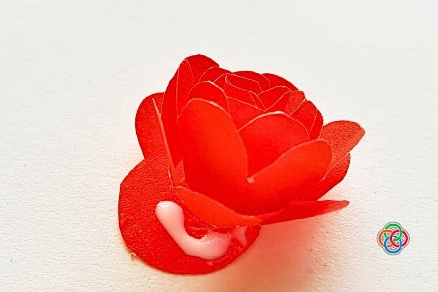 Red rose-shaped fondant decoration with a small white dollop at its base on a pale surface.