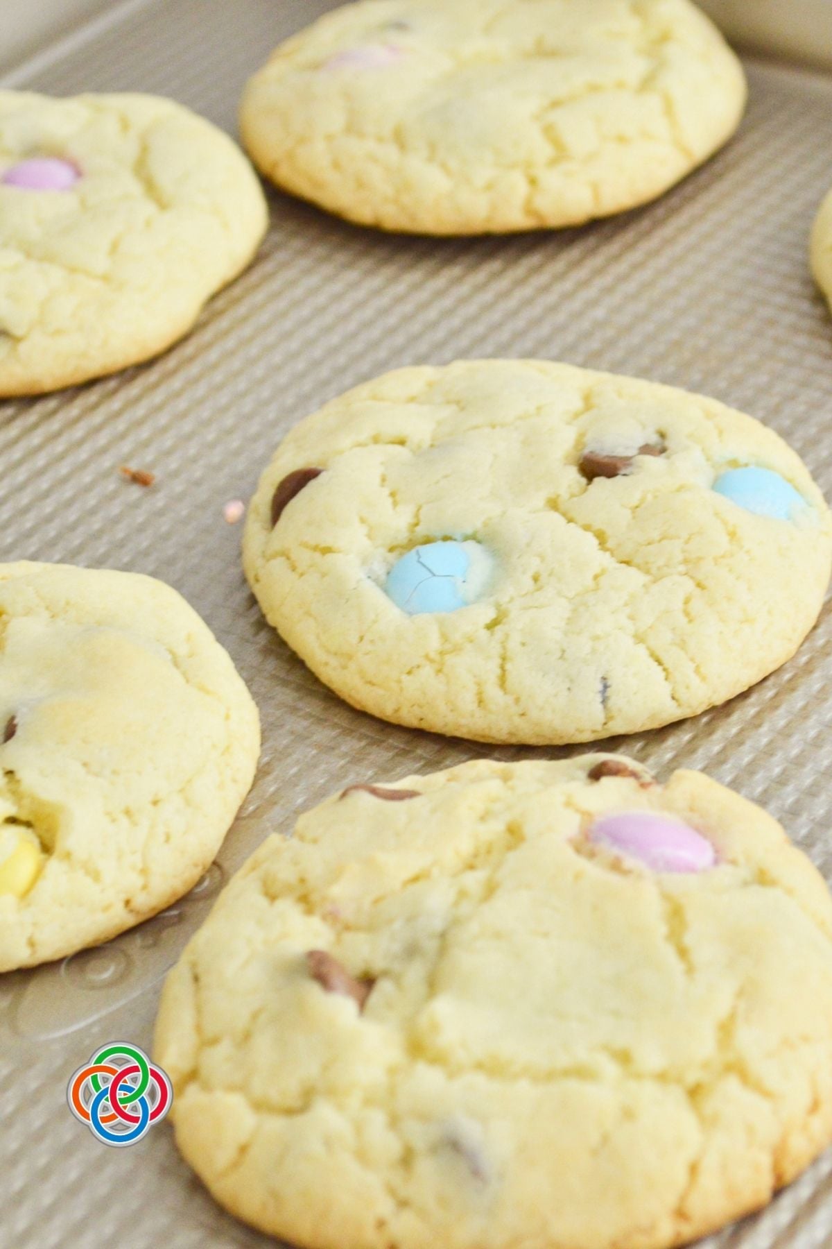 Freshly baked spring cake mix cookies with pastel M&M candies and chocolate chips on a baking sheet, showing soft texture and golden edges.
