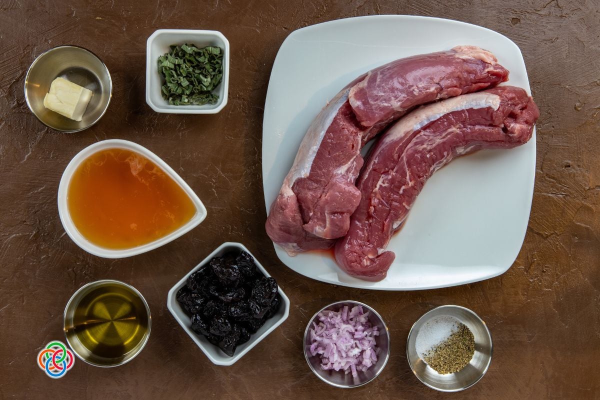 Ingredients for pork tenderloin with prune stuffing including raw pork, prunes, shallots, sage, butter, oil, and Irish ale arranged on a table.