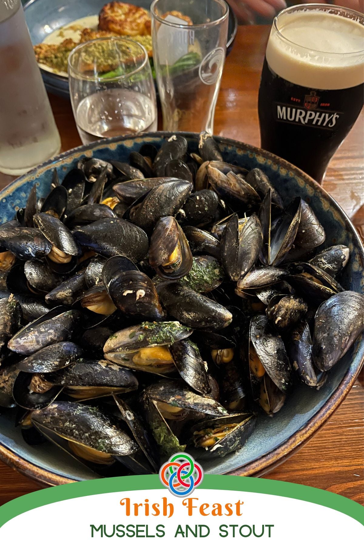 Bowl of cooked mussels served on a wooden table with a glass of Irish stout, labeled “Irish Feast Mussels and Stout.”
