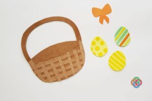 Paper Easter basket base with handle alongside colorful decorated paper eggs and a bow, ready to be assembled into a finished craft.