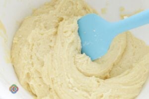 Thick cookie dough made from cake mix being mixed in a bowl with a blue spatula, showing smooth texture before adding mix-ins.