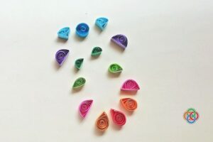 Colorful quilled paper shapes including coils and teardrops arranged on a plain background, ready to be used in an Easter egg craft design.