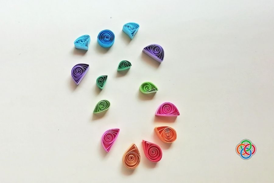 Colorful quilled paper shapes including coils and teardrops arranged on a plain background, ready to be used in an Easter egg craft design.