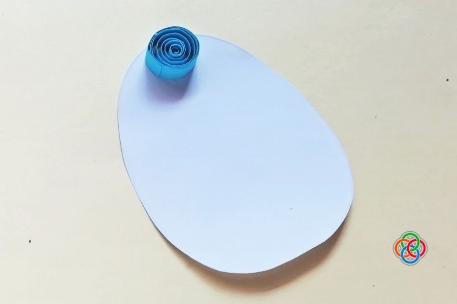 White egg-shaped paper template with a single blue quilled paper coil placed at the top, beginning an Easter craft design.