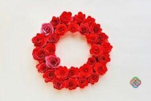 A completed circular wreath decorated with red and pink paper roses arranged closely together on a cardstock base, forming a full floral design.