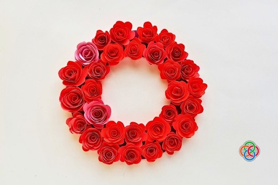 A completed circular wreath decorated with red and pink paper roses arranged closely together on a cardstock base, forming a full floral design.