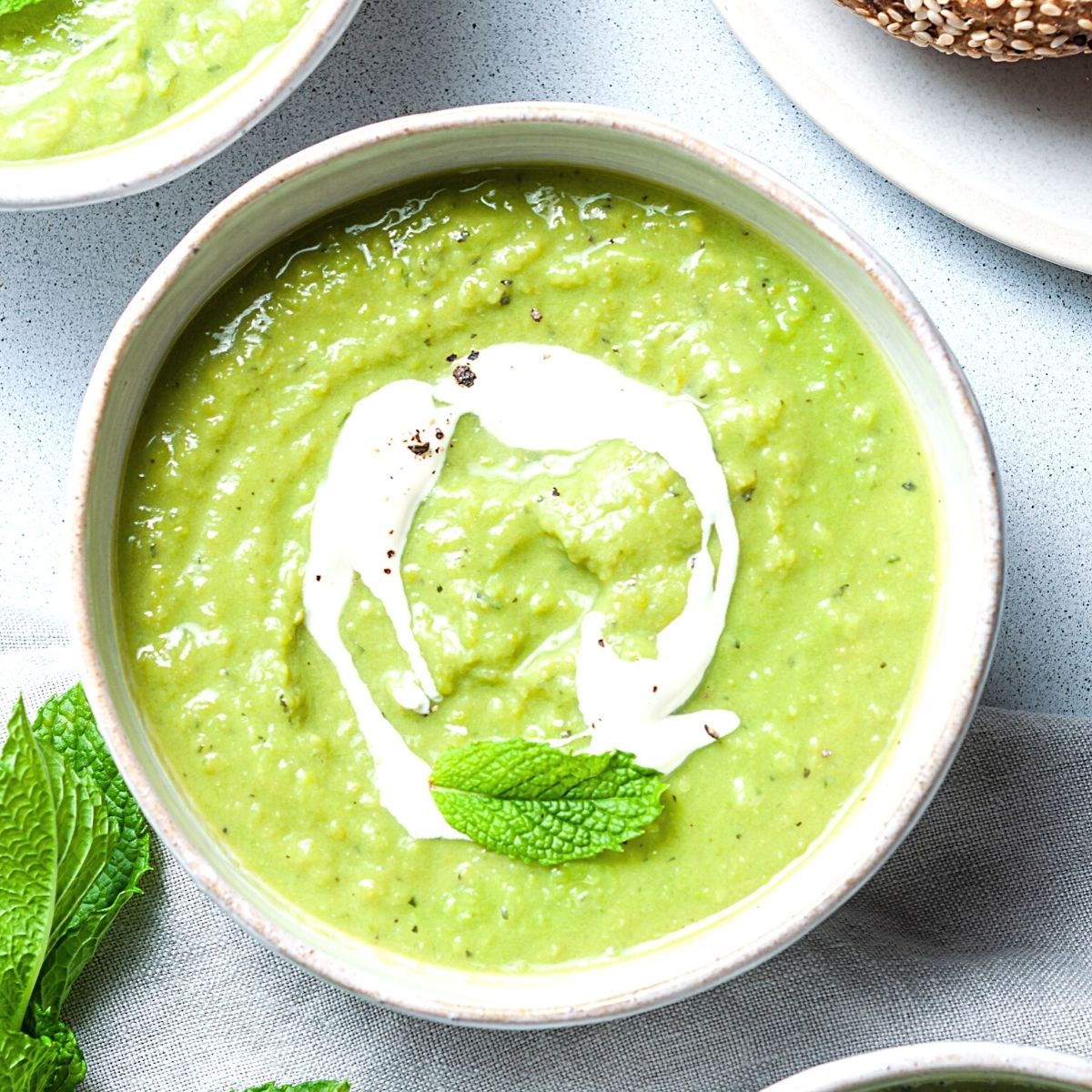 A bowl of bright green pea and mint soup topped with a swirl of cream and a fresh mint leaf.