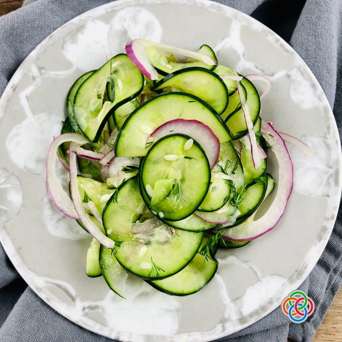 Pickled cucumber and onion salad with fresh dill on a white platter.