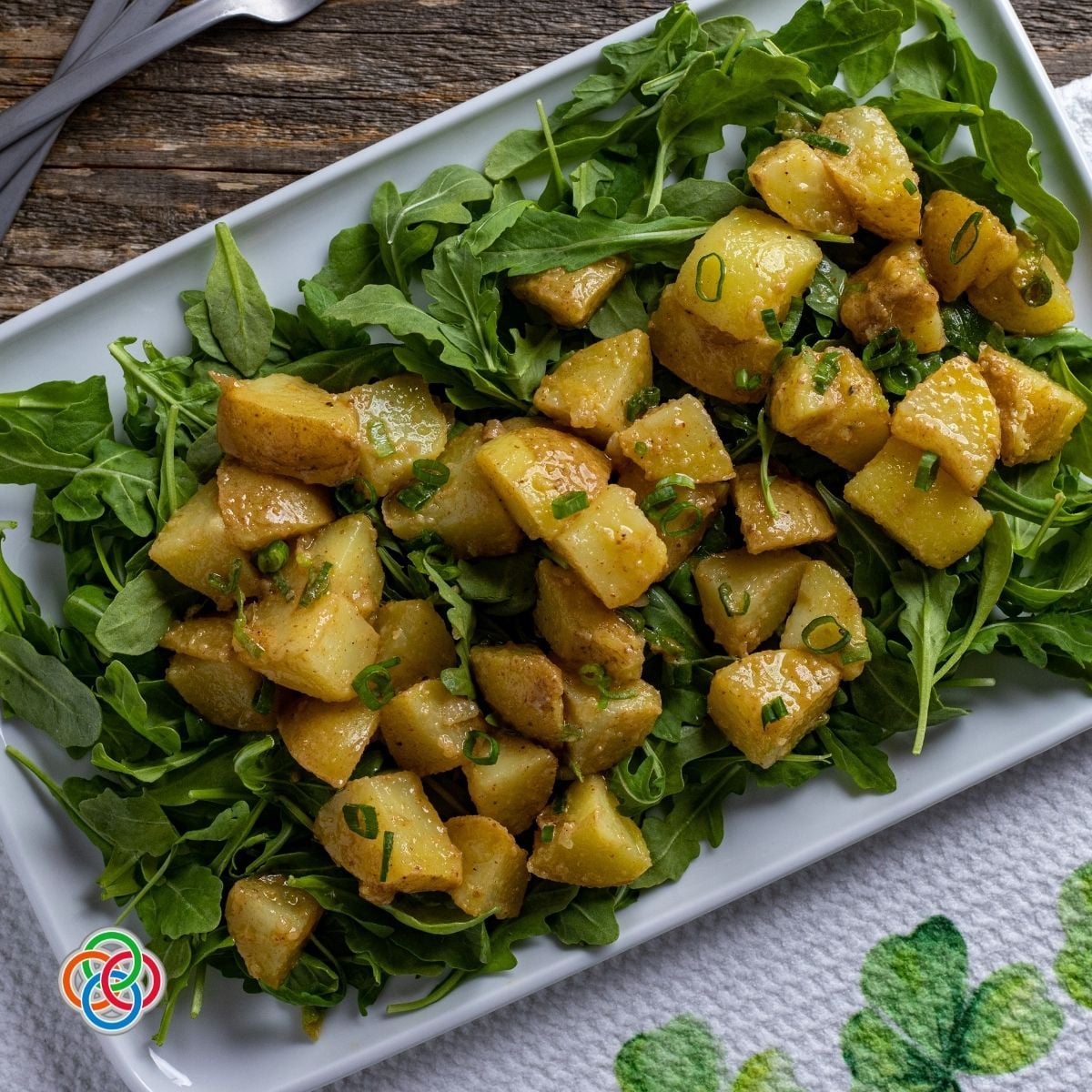 Potato salad mixed with fresh chives on a bed of greens on a white platter.