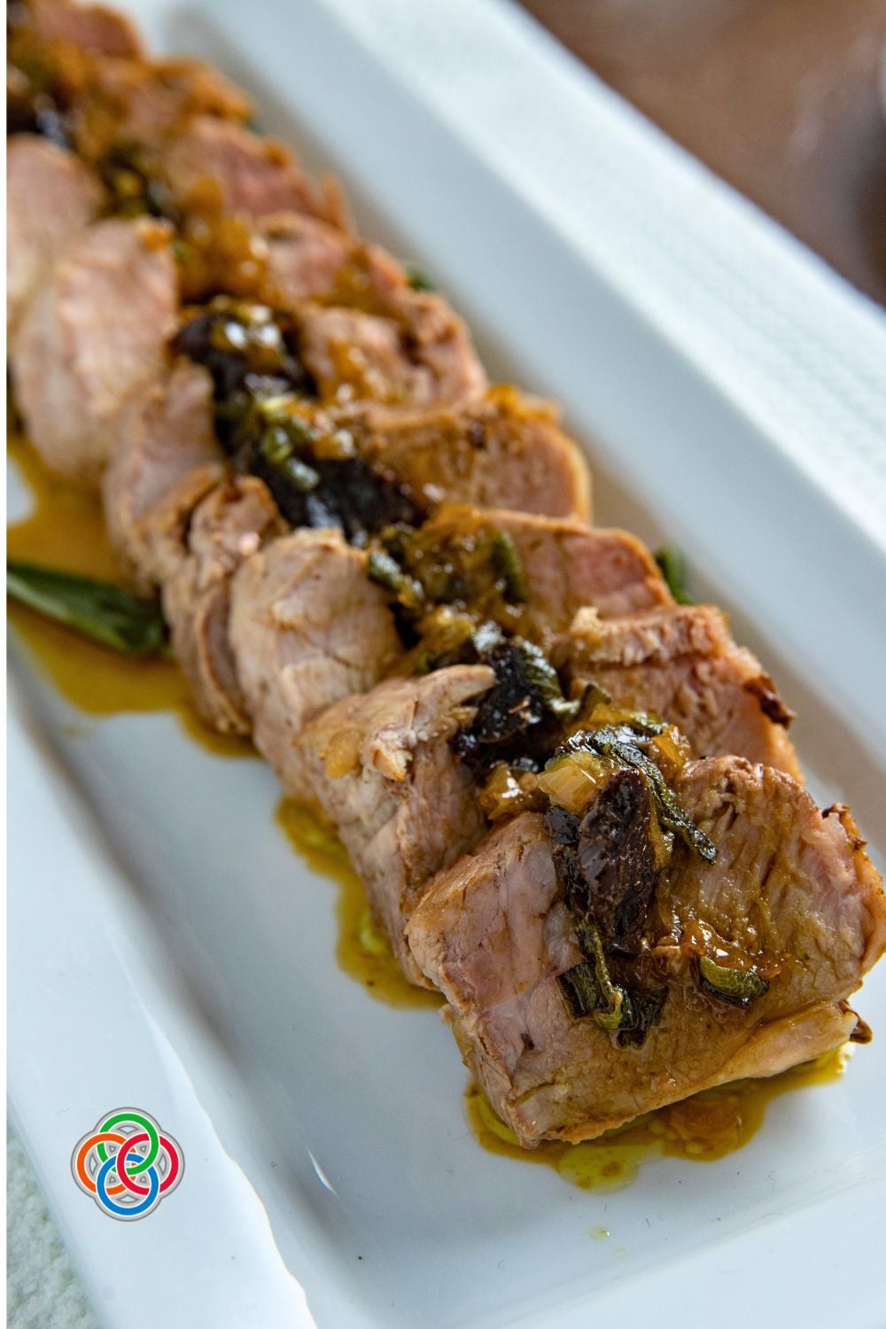 Sliced pork tenderloin stuffed with prunes and topped with savory gravy on a white serving platter.