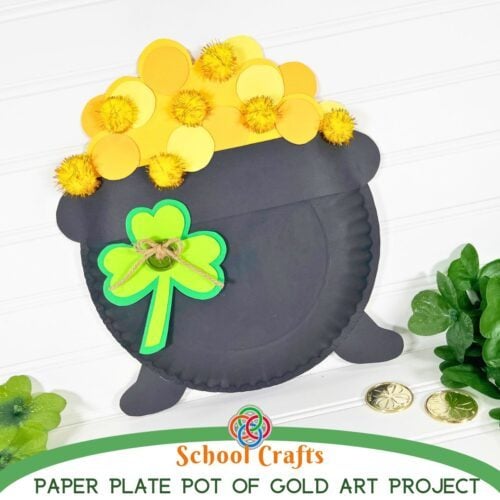 Completed paper plate pot of gold craft with yellow paper coins and gold pom poms, decorated with a green shamrock and twine bow, displayed with gold coins and greenery on a white background.