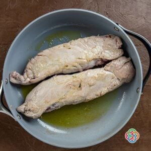 Searing the outside of stuffed pork steaks or tenderloins in a skillet | Irish American Mom Pork tenderloins searing in a skillet with oil, creating a golden crust for an Irish pork recipe.