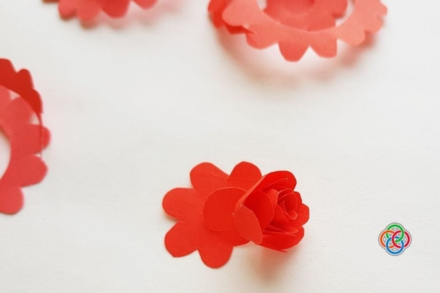 A red paper spiral rolled and shaped into a rose, with the base being secured to form a flower for a DIY wreath craft.