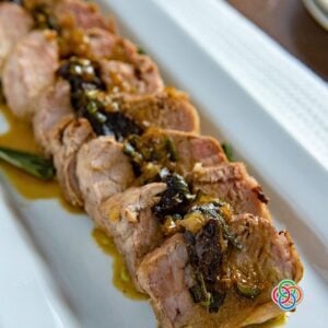 Sliced roasted pork tenderloin with prune stuffing | Irish American Mom Sliced roasted pork tenderloin with prune stuffing and pan juices served on a white platter.