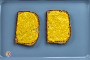 Two slices of wholemeal bread topped with a raw egg and grated cheese mixture on a baking tray, ready to be baked into egg and cheese toasts.