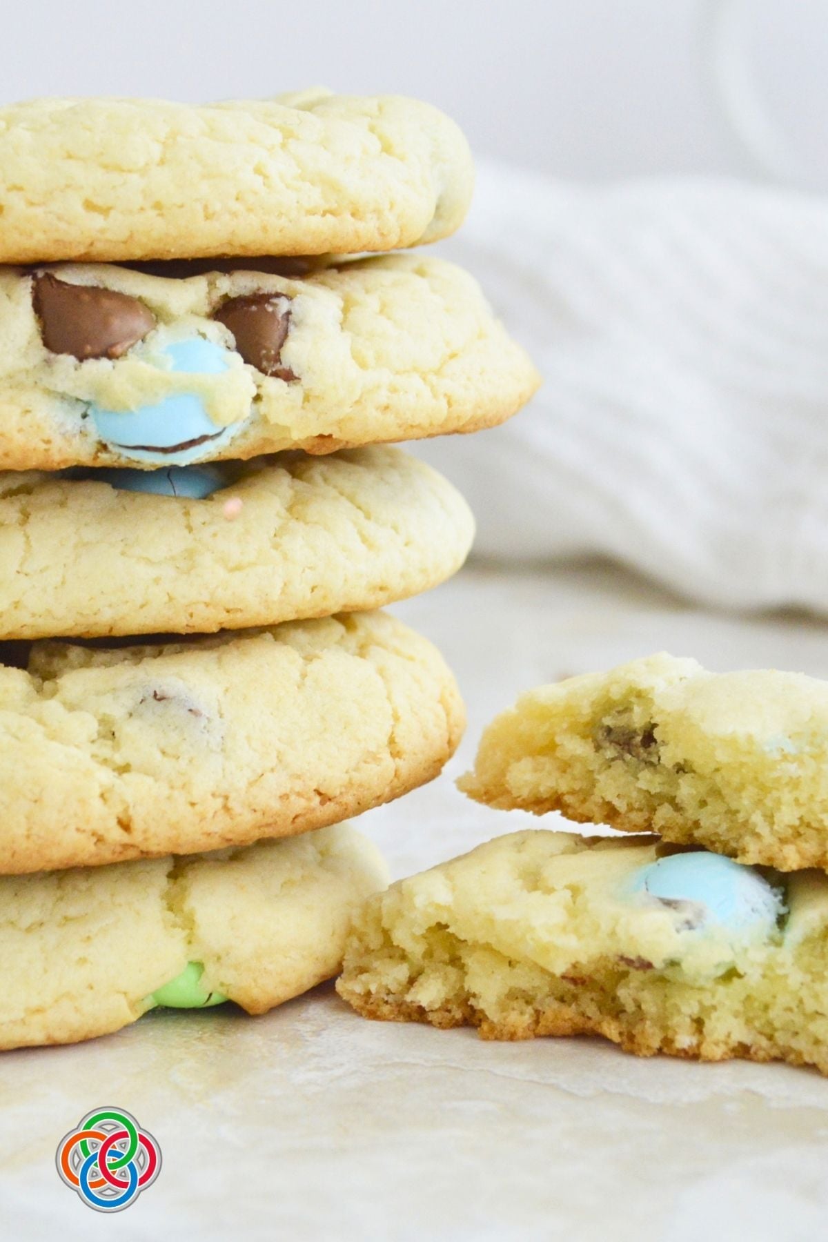 Stack of soft spring cake mix cookies with pastel M&M candies and chocolate chips, with one cookie broken open to show the chewy interior.