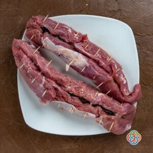Stuffied pork tenderloins held together with cocktail sticks | Irish American Mom Raw pork tenderloins stuffed with prunes and secured with cocktail sticks on a plate, ready for cooking.