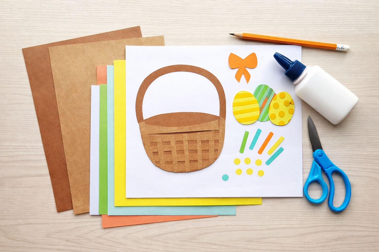 Overhead view of supplies for a paper Easter basket craft, including colored paper, brown cardstock basket pieces, decorated paper eggs, scissors, glue, and a pencil arranged on a light surface.